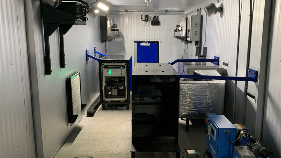 An interior view of a compact room with various equipment and machinery arranged along the walls and floor.